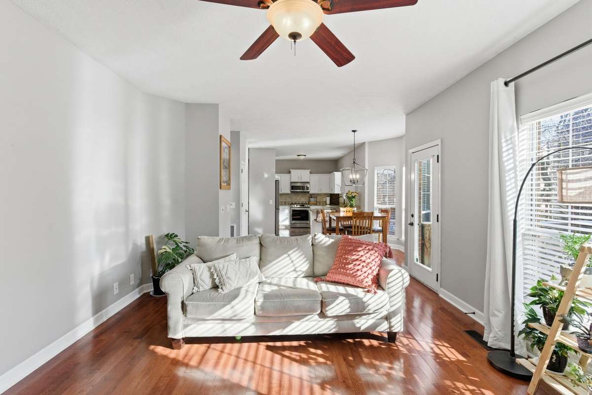 Light-filled living room with hardwood floors, ceiling fan, and a classic fireplace, offering flexible space for a media room, or additional gathering area while maintaining an open flow to the main living spaces.