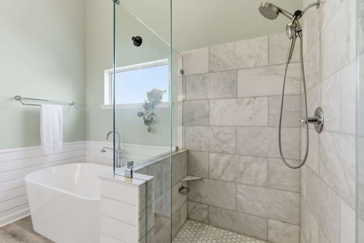 Spa-inspired owner’s bathroom featuring a freestanding soaking tub, glass-enclosed tiled shower, dual vanities with marble countertops, and abundant natural light—designed for everyday ease and quiet luxury.