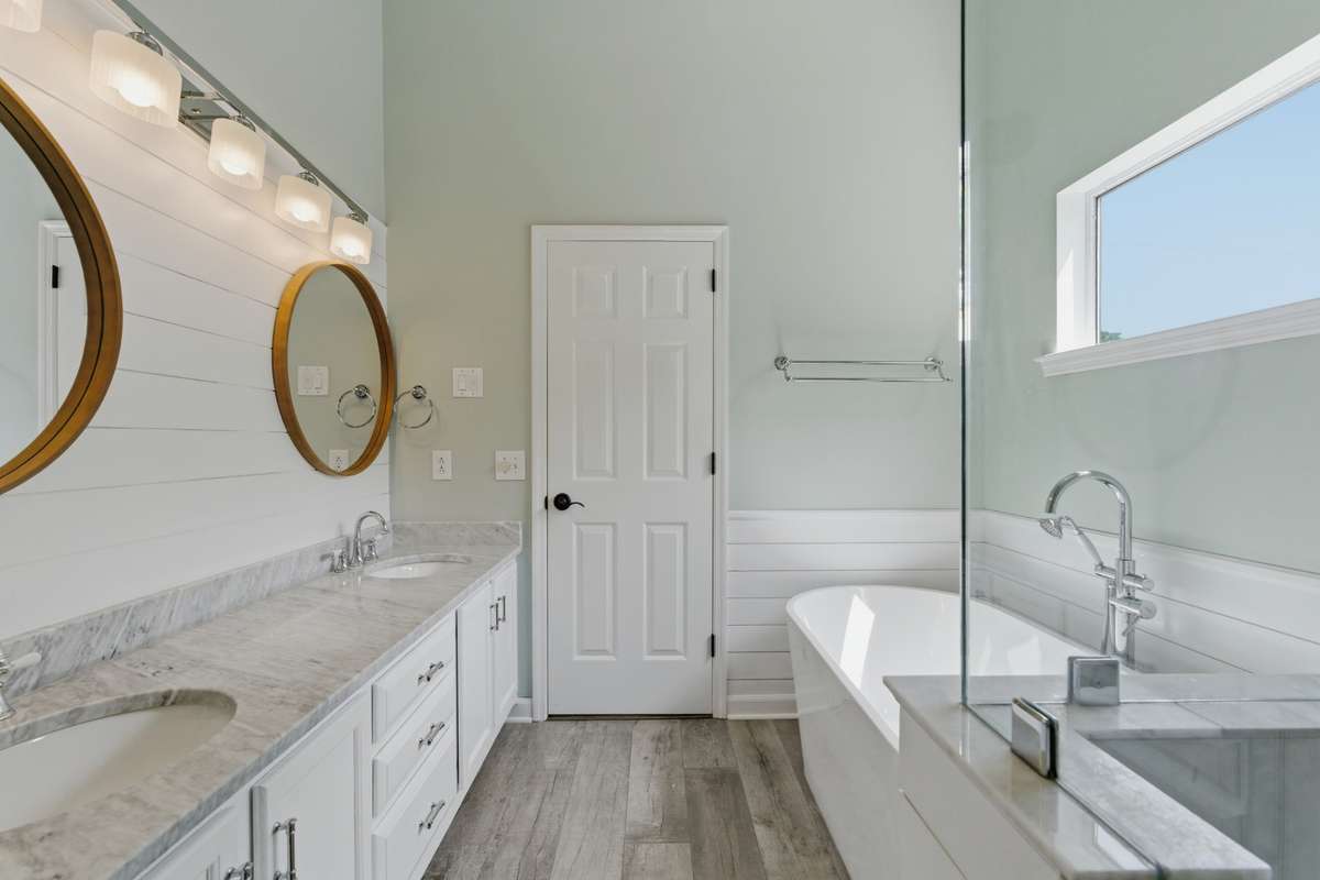 Spa-inspired owner’s bathroom featuring a freestanding soaking tub, glass-enclosed tiled shower, dual vanities with marble countertops, and abundant natural light—designed for everyday ease and quiet luxury.