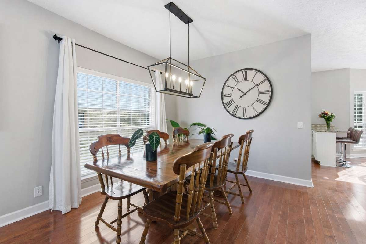 Formal dining room with warm hardwood floors, modern chandelier, and abundant natural light. An inviting space for hosting gatherings or everyday meals, seamlessly connected to the main living areas.