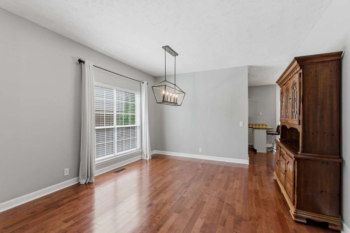 Formal dining room with warm hardwood floors, modern chandelier, and abundant natural light. An inviting space for hosting gatherings or everyday meals, seamlessly connected to the main living areas.