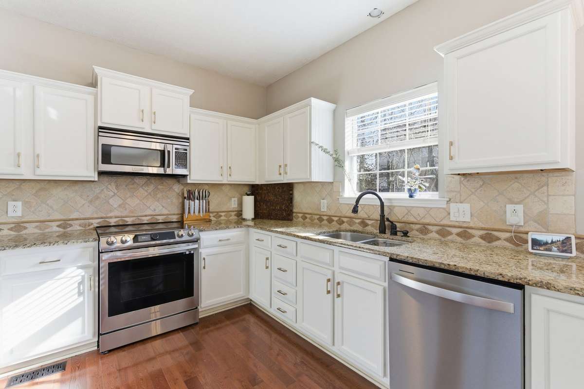 Bright, updated kitchen featuring white cabinetry, granite countertops, and new high-end stainless appliances, including an induction range with air-fry capability. Designed for both everyday function and effortless entertaining.