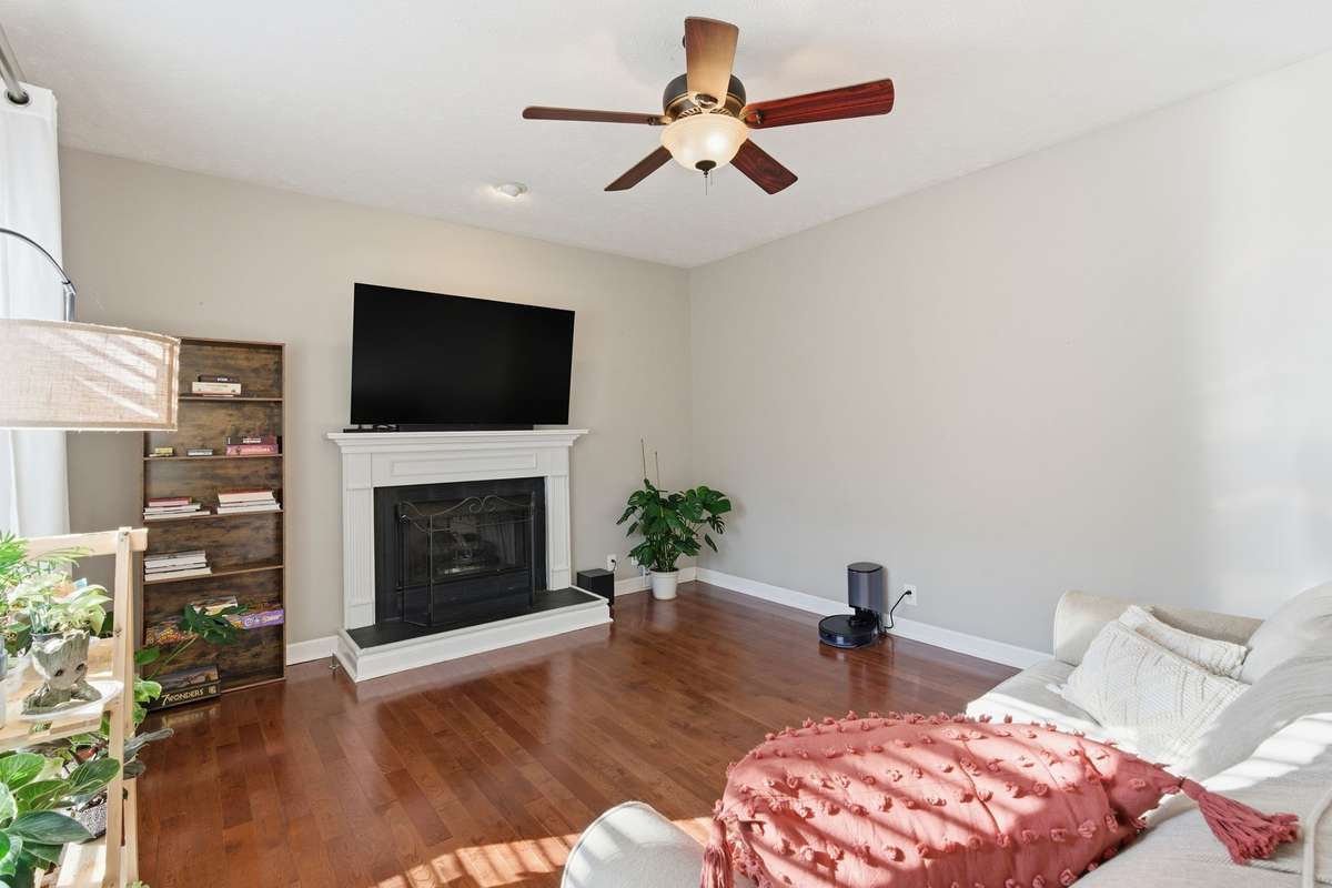 Light-filled living room with hardwood floors, ceiling fan, and a classic fireplace, offering flexible space for a media room, or additional gathering area while maintaining an open flow to the main living spaces.
