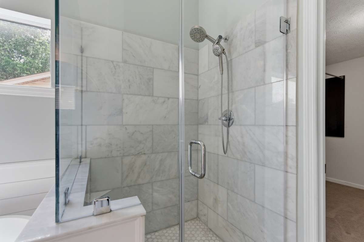 Spa-inspired owner’s bathroom featuring a freestanding soaking tub, glass-enclosed tiled shower, dual vanities with marble countertops, and abundant natural light—designed for everyday ease and quiet luxury.