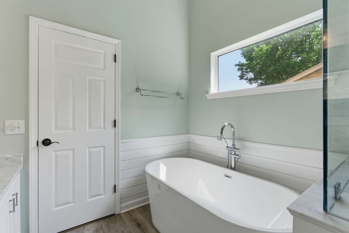 Spa-inspired owner’s bathroom featuring a freestanding soaking tub, glass-enclosed tiled shower, dual vanities with marble countertops, and abundant natural light—designed for everyday ease and quiet luxury.