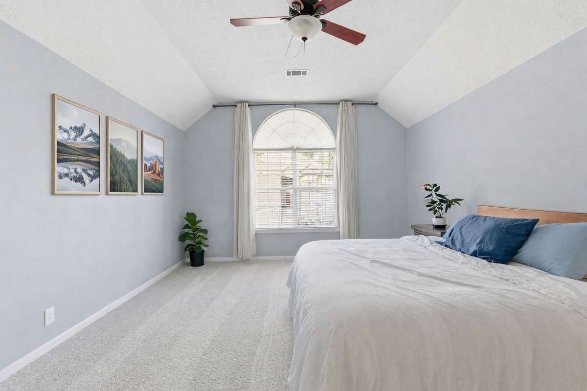 Light-filled owner’s bedroom with vaulted ceilings, soft neutral tones, and an arched window. Directly connected to the owner’s bathroom and walk-in closet for comfort, privacy, and everyday ease. - Virtually staged