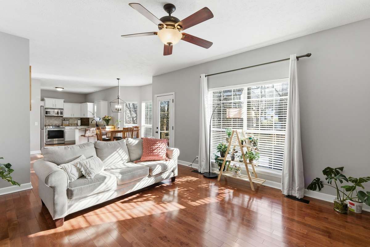 Light-filled living room with hardwood floors, ceiling fan, and a classic fireplace, offering flexible space for a media room, or additional gathering area while maintaining an open flow to the main living spaces.
