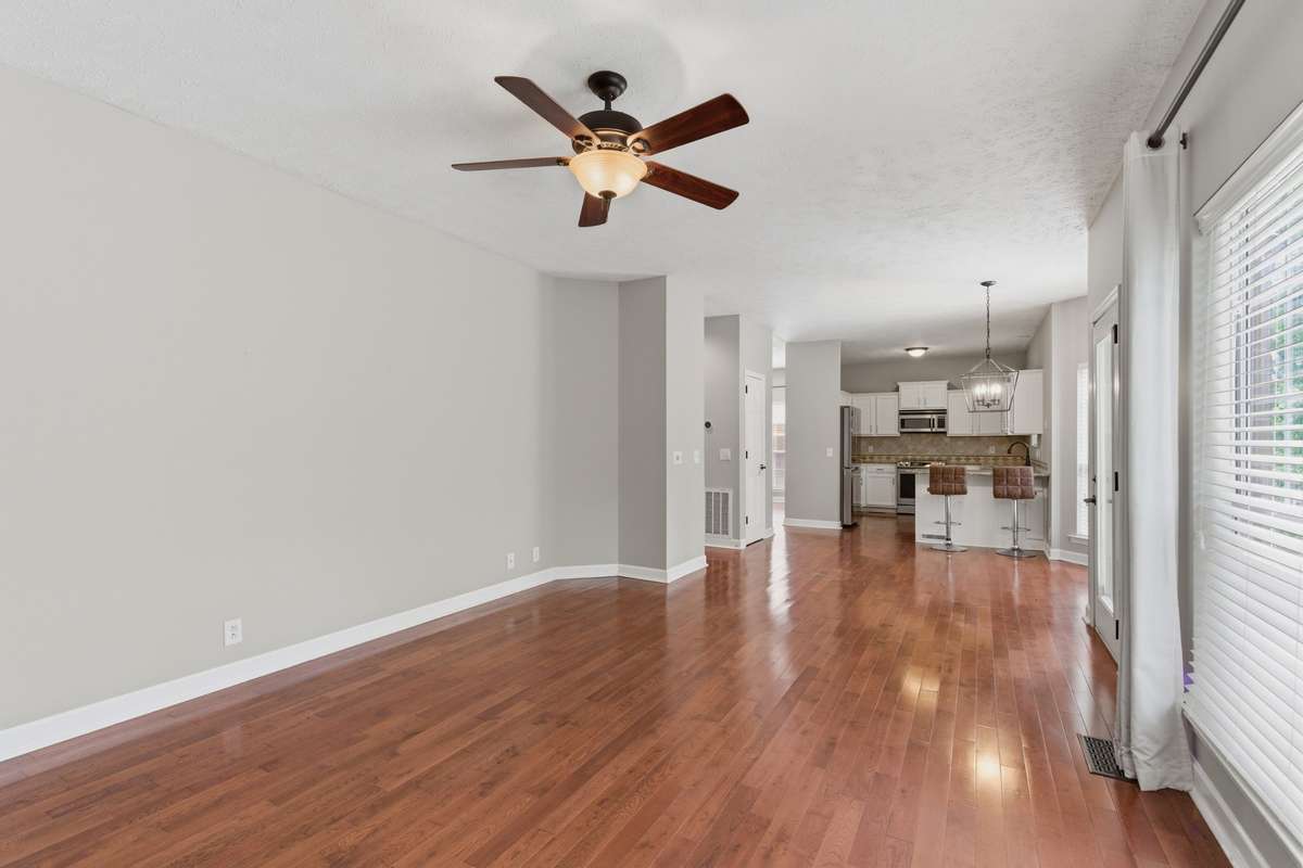 Light-filled living room with hardwood floors, ceiling fan, and a classic fireplace, offering flexible space for a media room, or additional gathering area while maintaining an open flow to the main living spaces.