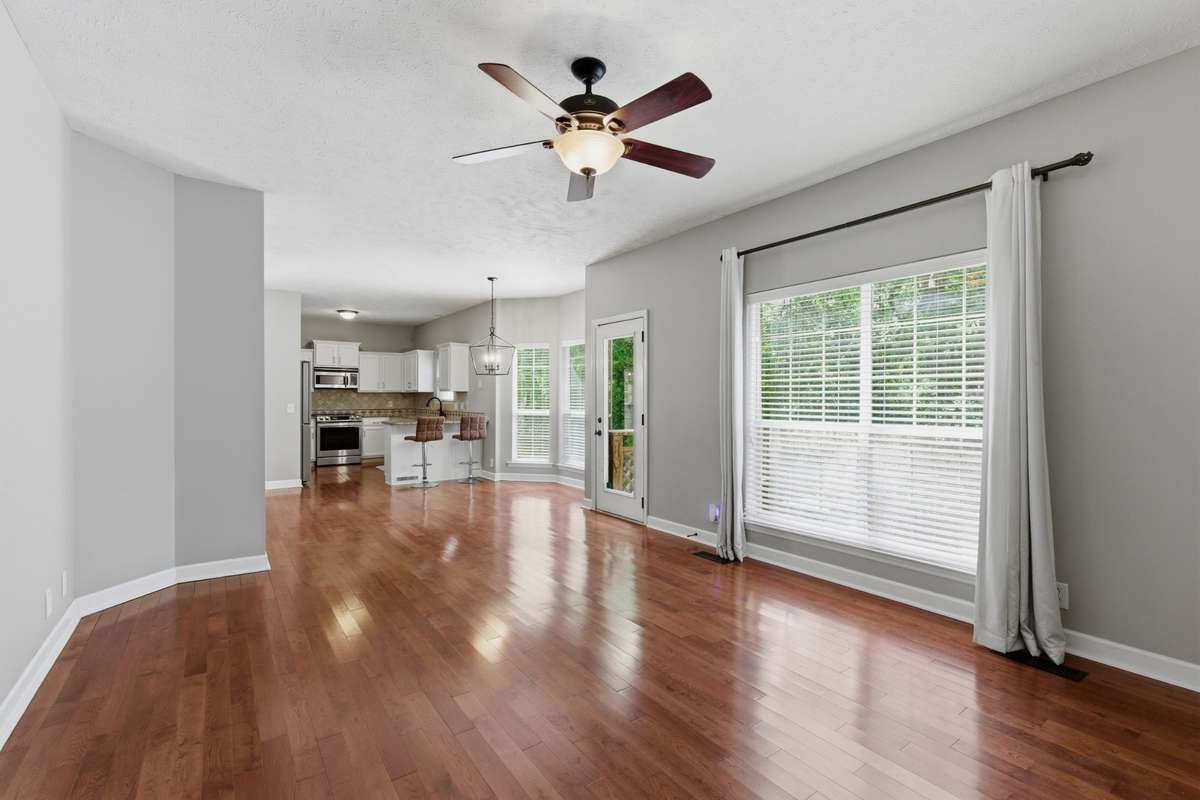 Light-filled living room with hardwood floors, ceiling fan, and a classic fireplace, offering flexible space for a media room, or additional gathering area while maintaining an open flow to the main living spaces.