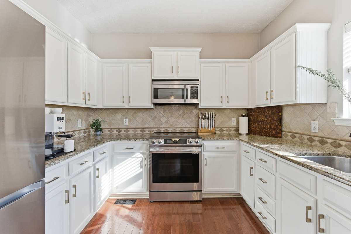 Bright, updated kitchen featuring white cabinetry, granite countertops, and new high-end stainless appliances, including an induction range with air-fry capability. Designed for both everyday function and effortless entertaining.