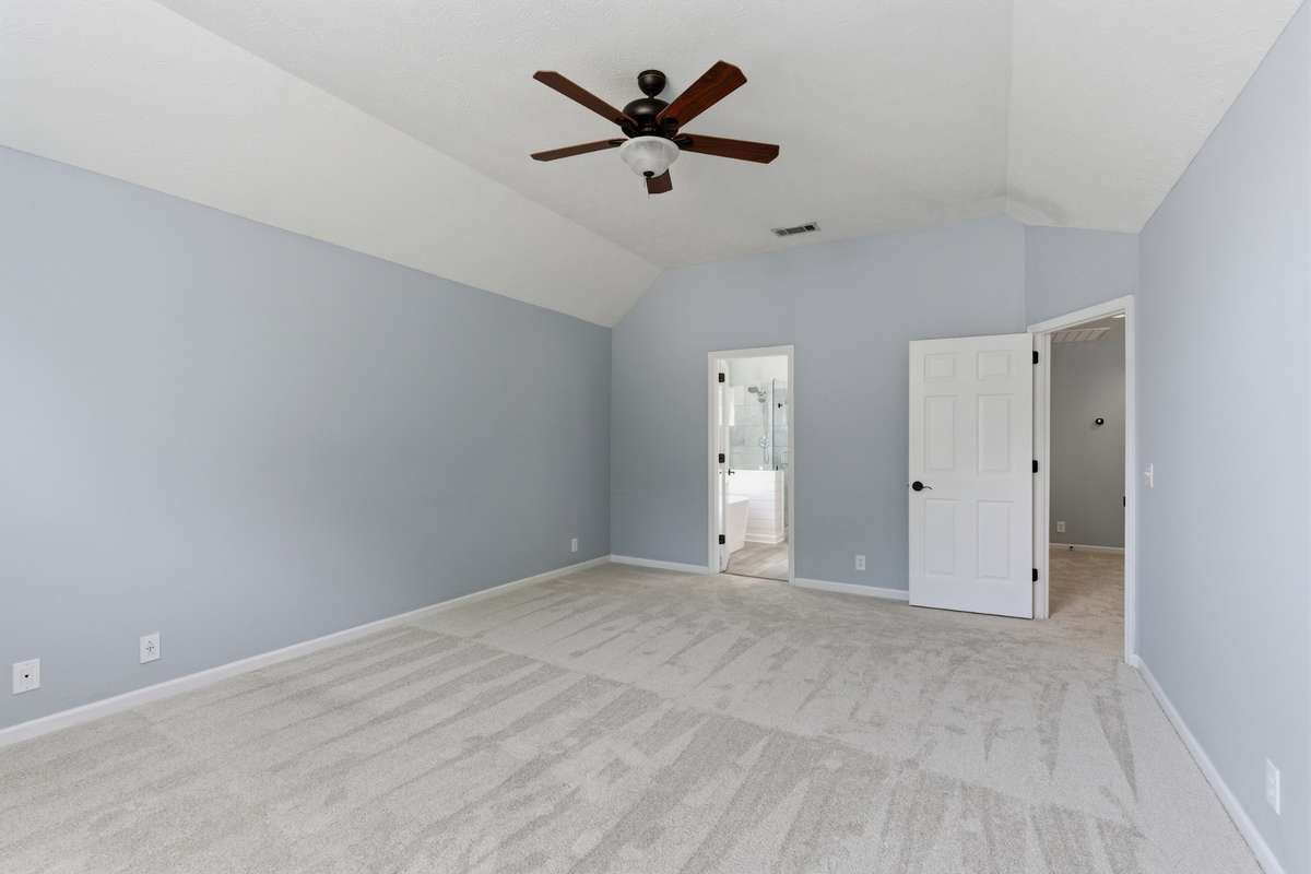 Light-filled owner’s bedroom with vaulted ceilings, soft neutral tones, and an arched window. Directly connected to the owner’s bathroom and walk-in closet for comfort, privacy, and everyday ease.