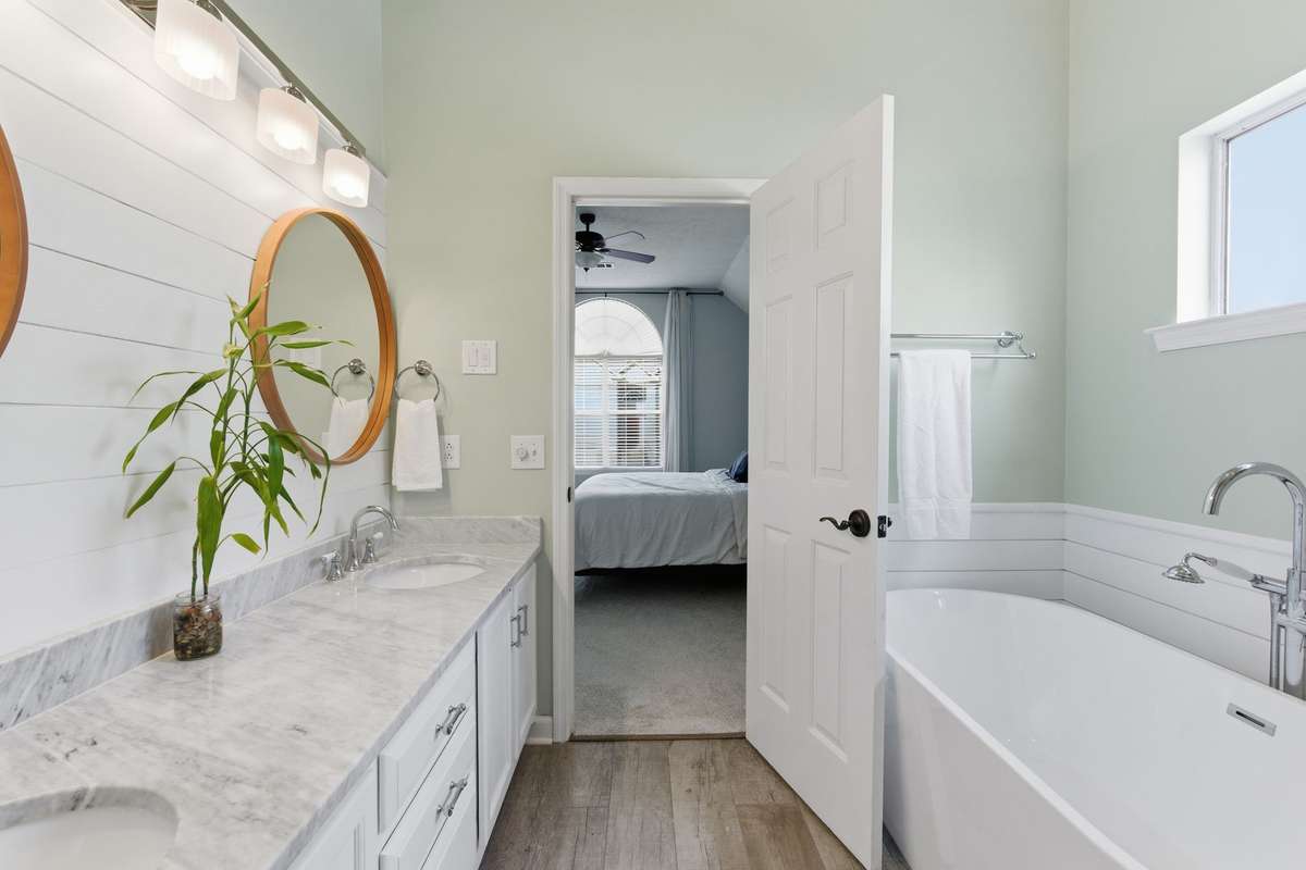 Spa-inspired owner’s bathroom featuring a freestanding soaking tub, glass-enclosed tiled shower, dual vanities with marble countertops, and abundant natural light—designed for everyday ease and quiet luxury.