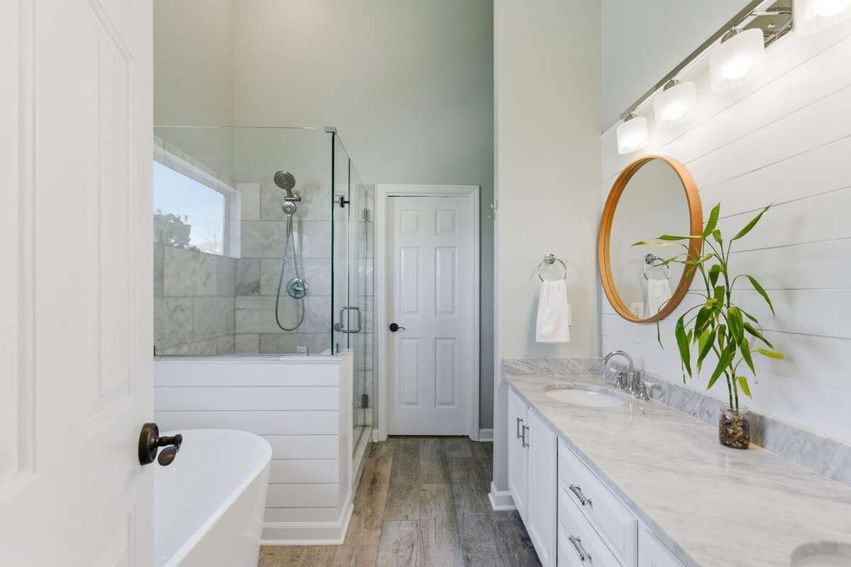 Spa-inspired owner’s bathroom featuring a freestanding soaking tub, glass-enclosed tiled shower, dual vanities with marble countertops, and abundant natural light—designed for everyday ease and quiet luxury.