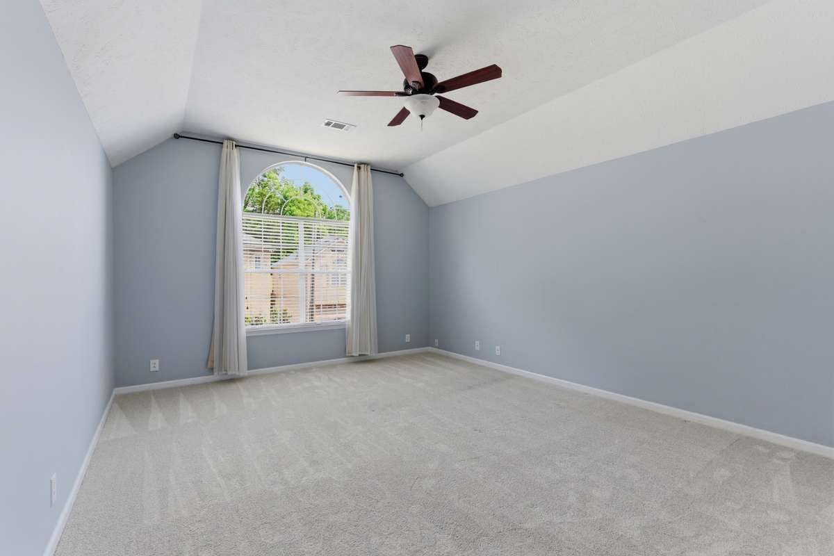 Light-filled owner’s bedroom with vaulted ceilings, soft neutral tones, and an arched window. Directly connected to the owner’s bathroom and walk-in closet for comfort, privacy, and everyday ease.