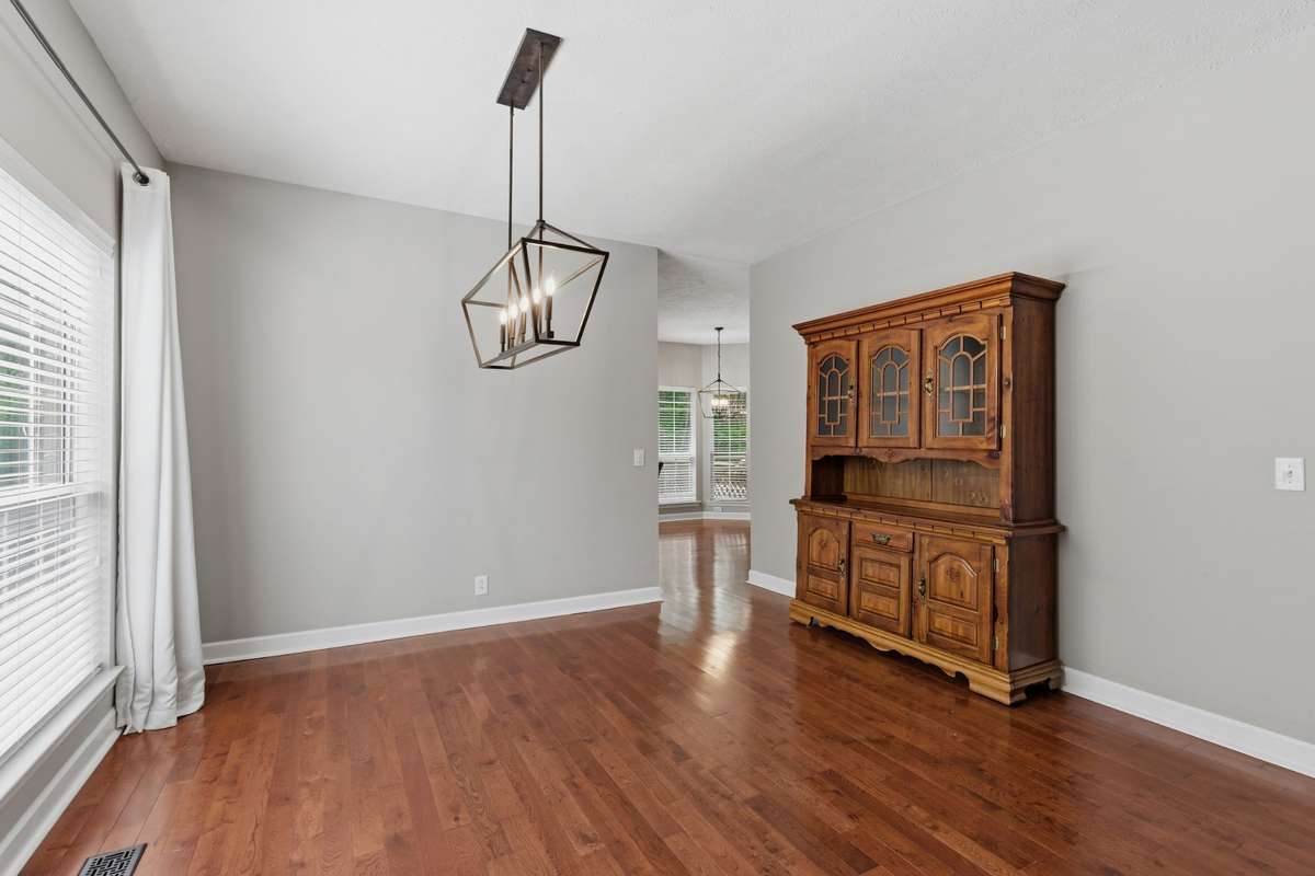 Formal dining room with warm hardwood floors, modern chandelier, and abundant natural light. An inviting space for hosting gatherings or everyday meals, seamlessly connected to the main living areas.