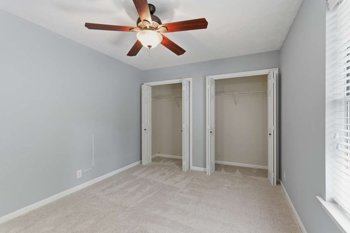 Bright second bedroom with plush carpet, ceiling fan, and generous closet space—ideal for a guest room, home office, or flex space with natural light and a quiet second-level setting.