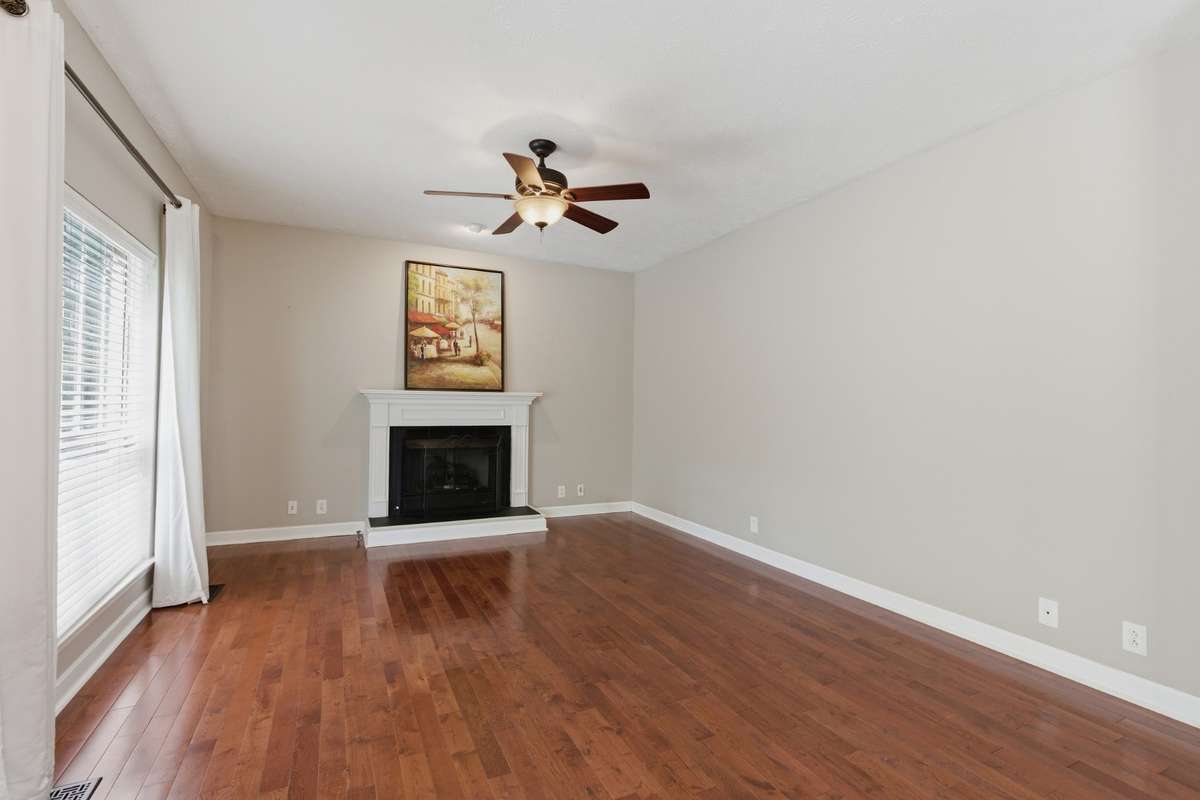 Light-filled living room with hardwood floors, ceiling fan, and a classic fireplace, offering flexible space for a media room, or additional gathering area while maintaining an open flow to the main living spaces.
