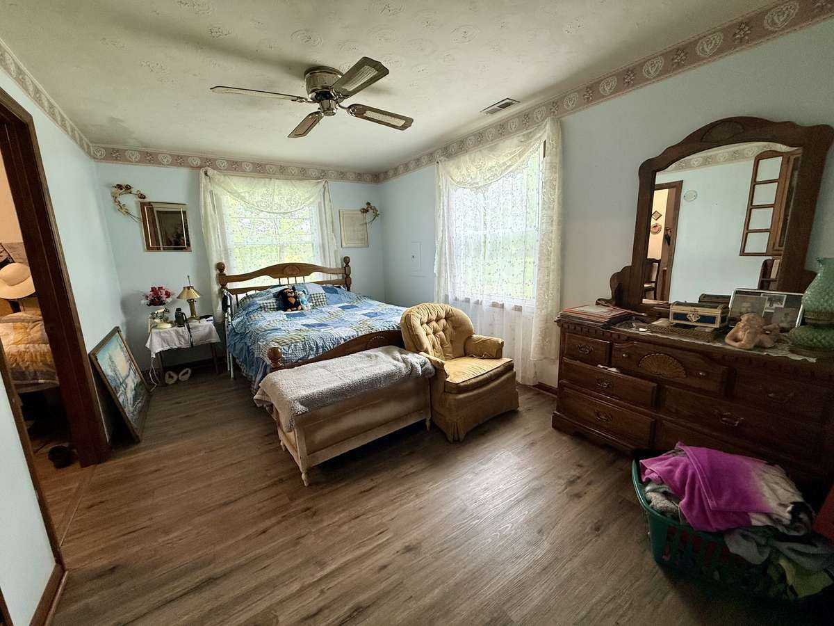 Primary bedroom with vinyl flooring, ceiling fan and sunny windows.