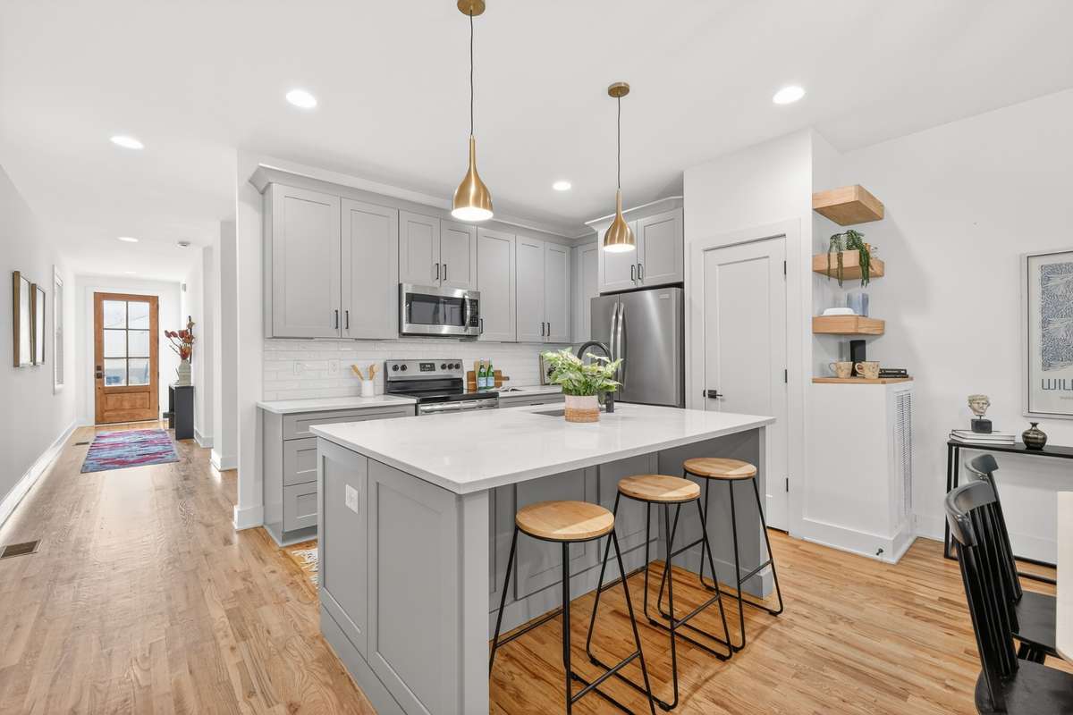 View from the dining area into towards the front of the house into the kichen. You can see the kitchen pantry and seating built into the island. Soft-close cabinets. Stainless steel French Door three drawer Refrigerator.