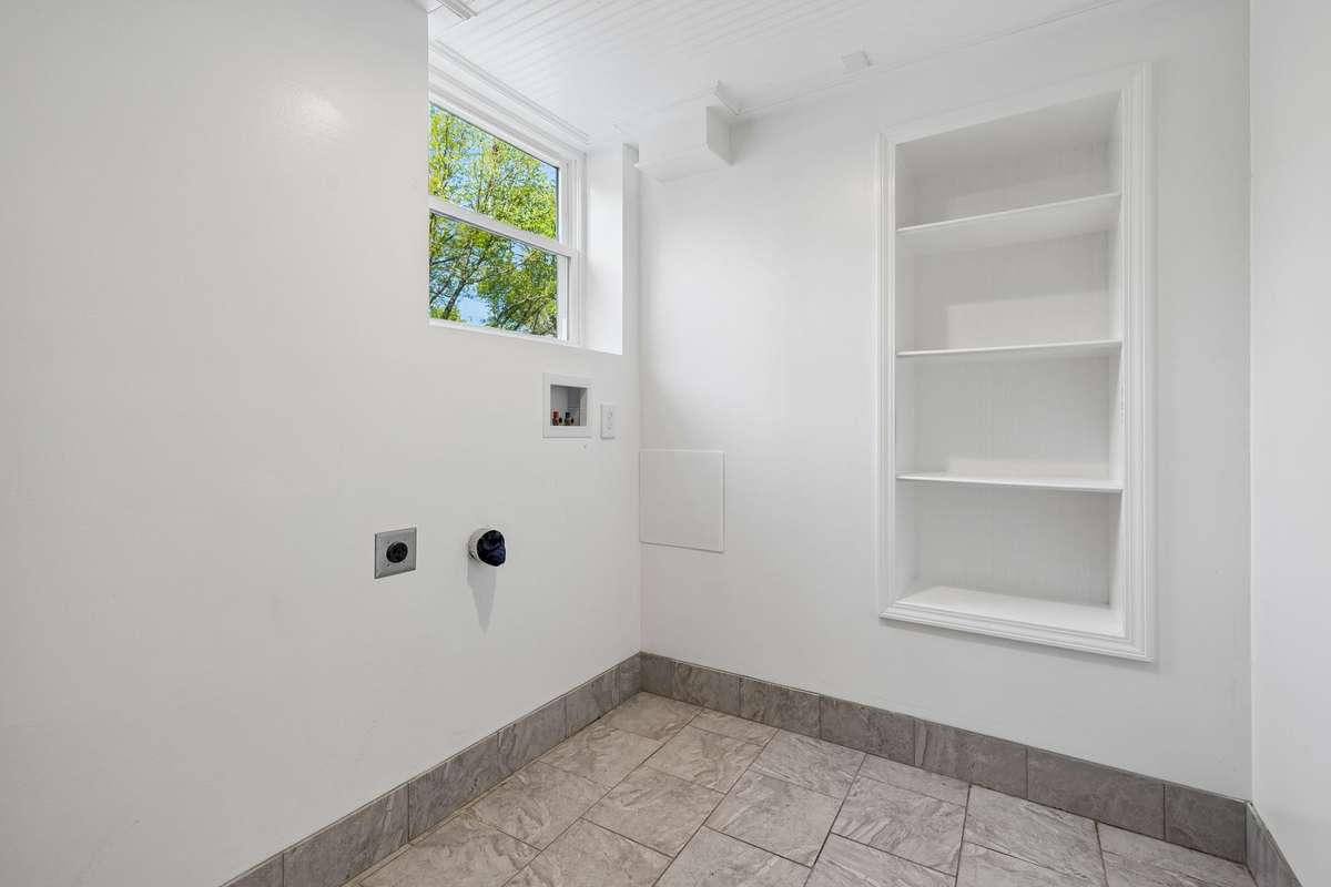 Sophisticated laundry room with elegant crown molding, detailed ceiling, and custom built-in shelves. Tiled floors add beauty and durability to this well-appointed space.