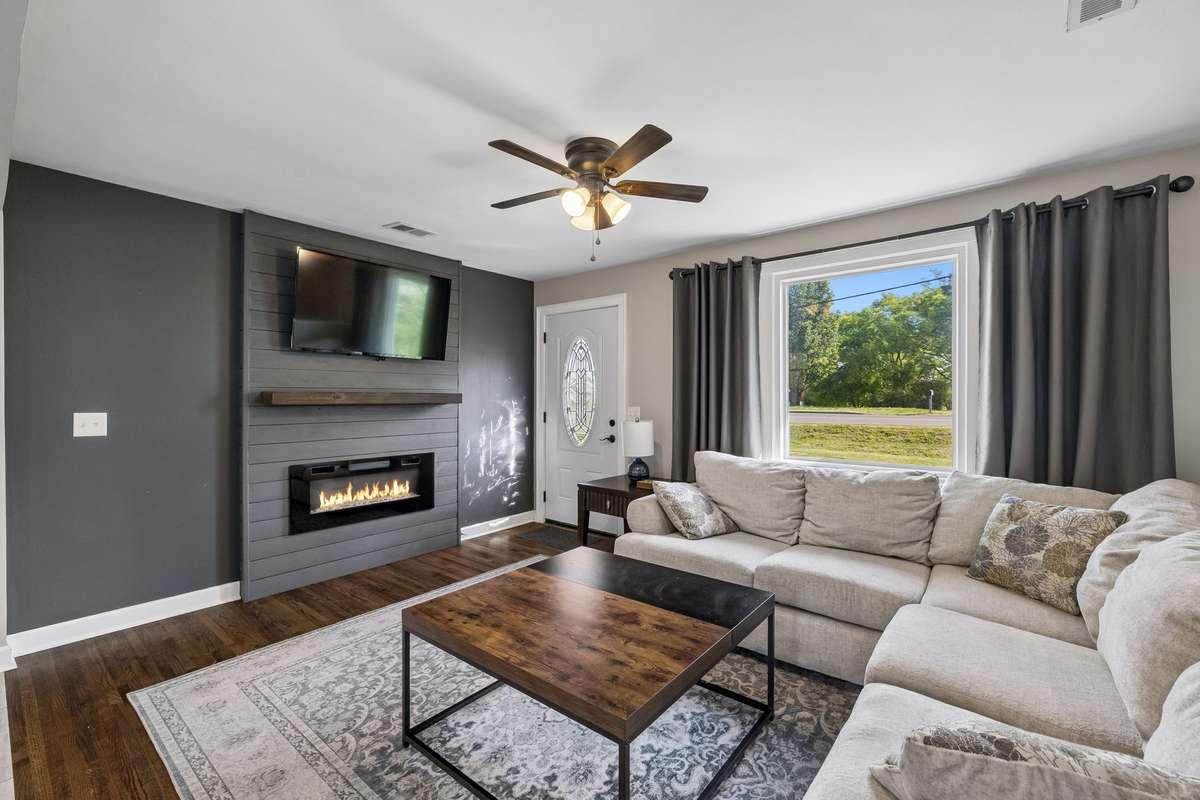 The living room features a stunning, detailed shiplap accent wall with a large mounted TV and a cozy electric fireplace, creating the perfect space for relaxing and entertaining.