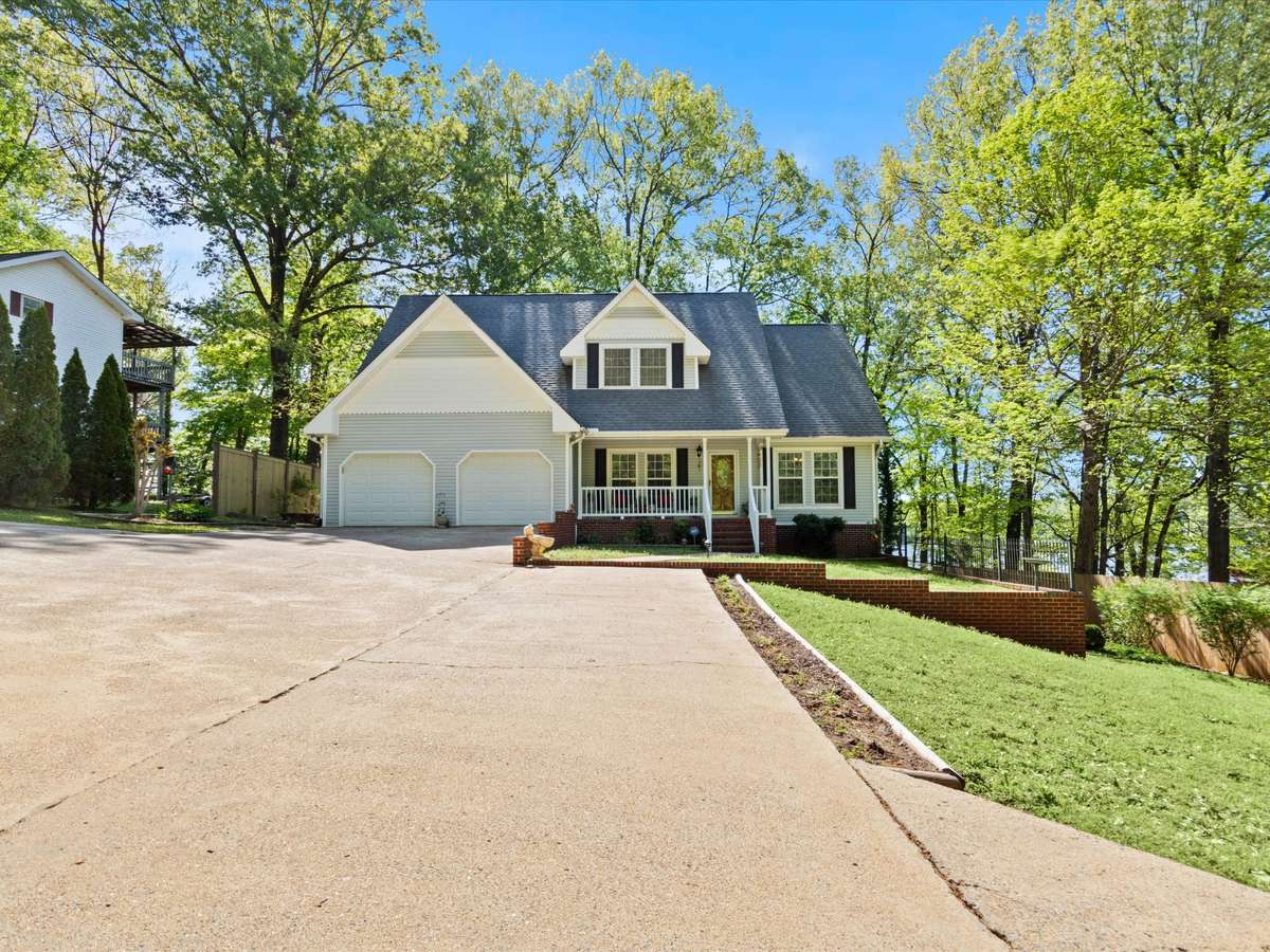 Front of house- Vinyl house, concrete driveway and sidewalks, covered front porch with railing and home entry, two car attached garage, shaded yard beautifully maintained yard