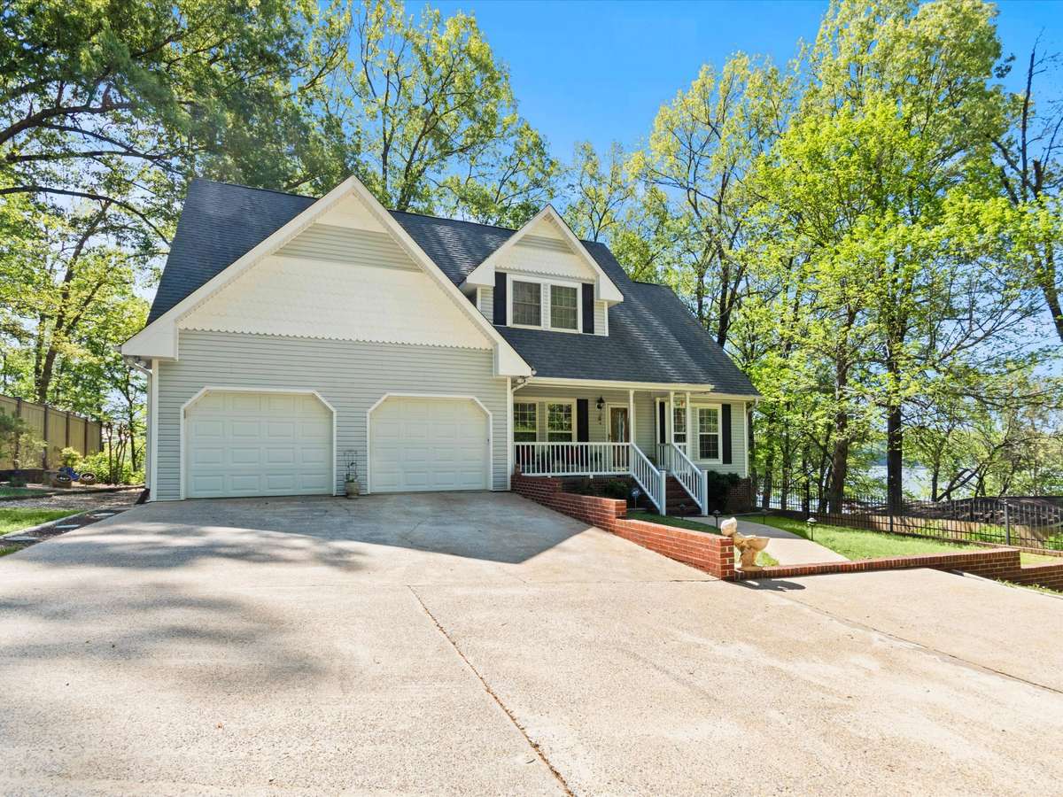Front of house- Vinyl house, concrete driveway and sidewalks, covered front porch with railing and home entry, two car attached garage, shaded yard beautifully maintained yard