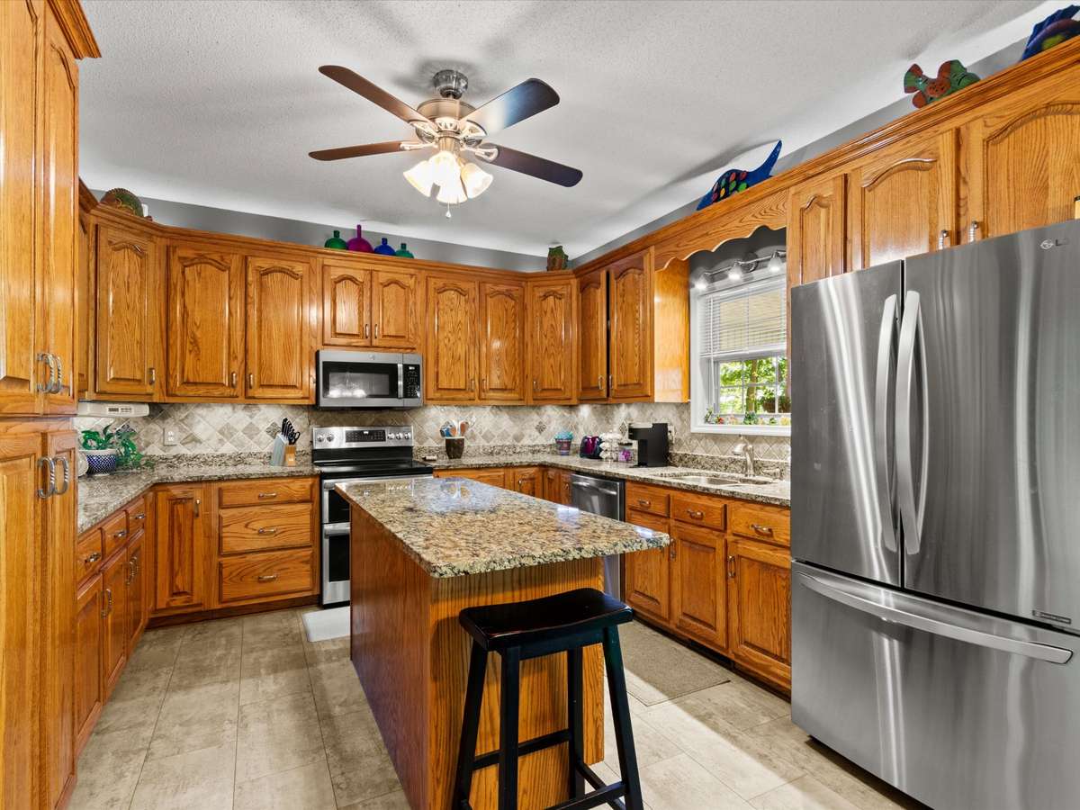 Kitchen- LVP flooring, wood cabinetry, tile backsplash, ceiling fan, stainless steel appliances, 9' ceilings