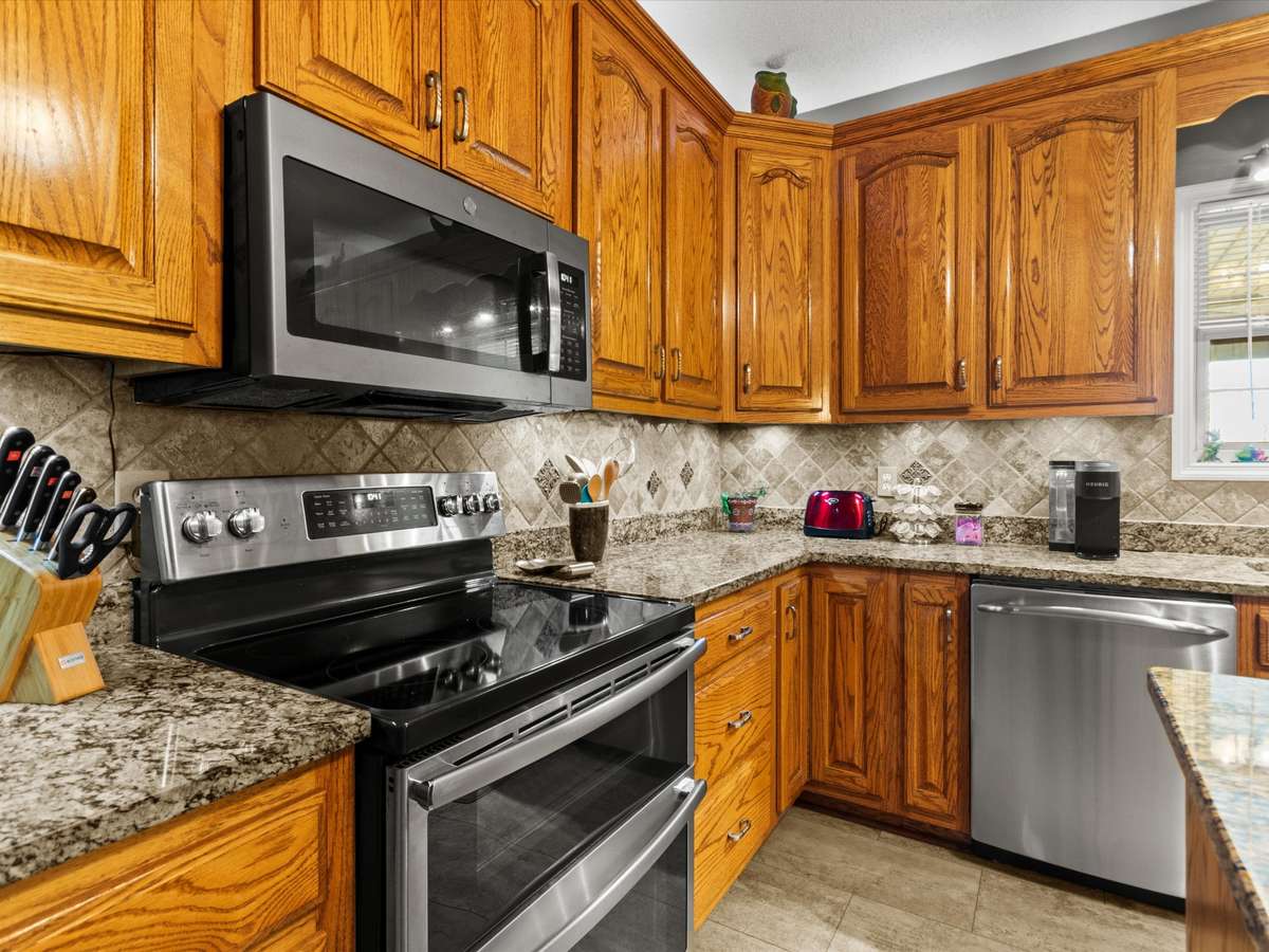 Kitchen- LVP flooring, wood cabinetry, tile backsplash, ceiling fan, stainless steel appliances, 9' ceilings