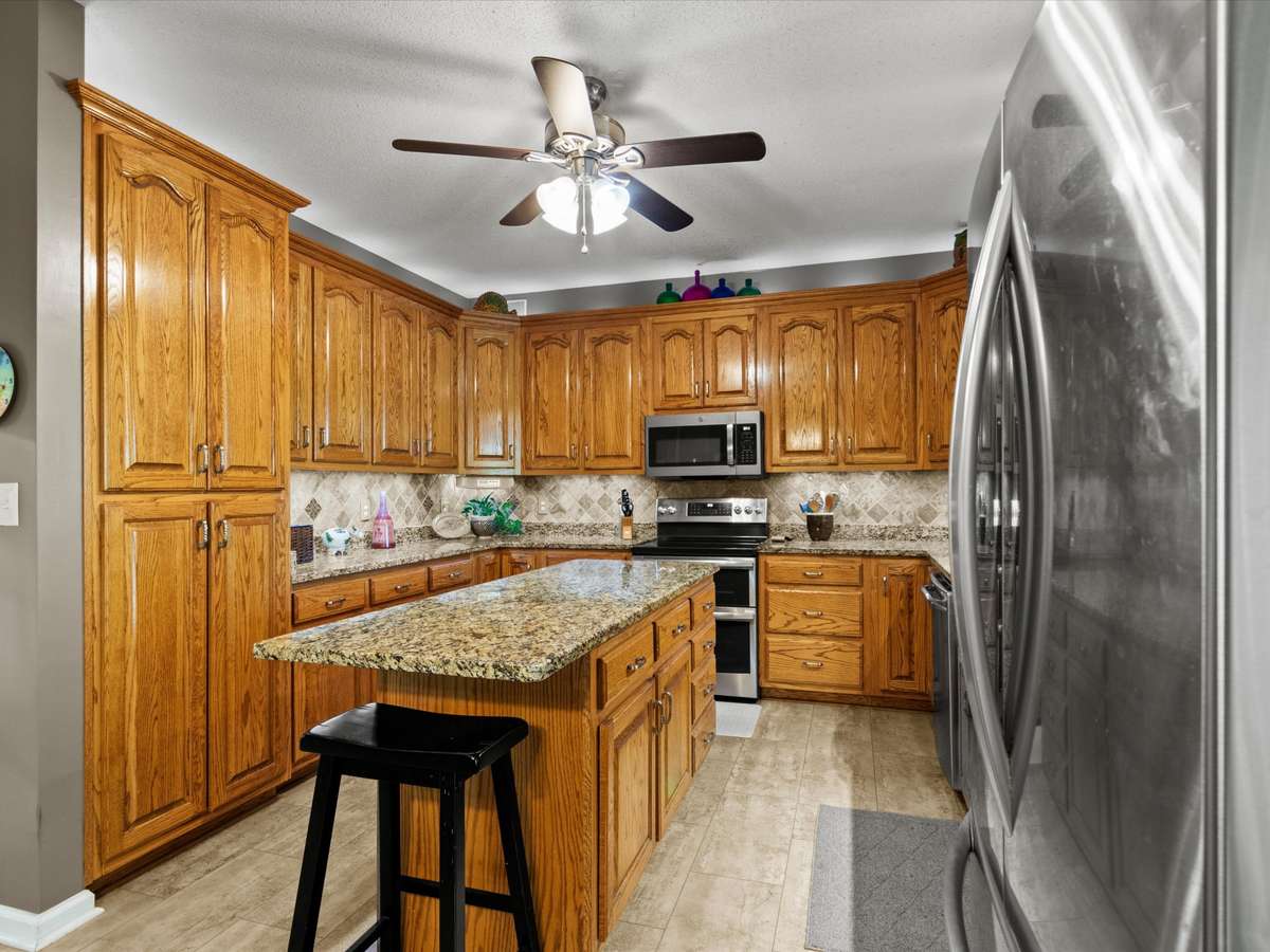 Kitchen- LVP flooring, wood cabinetry, tile backsplash, ceiling fan, stainless steel appliances, 9' ceilings
