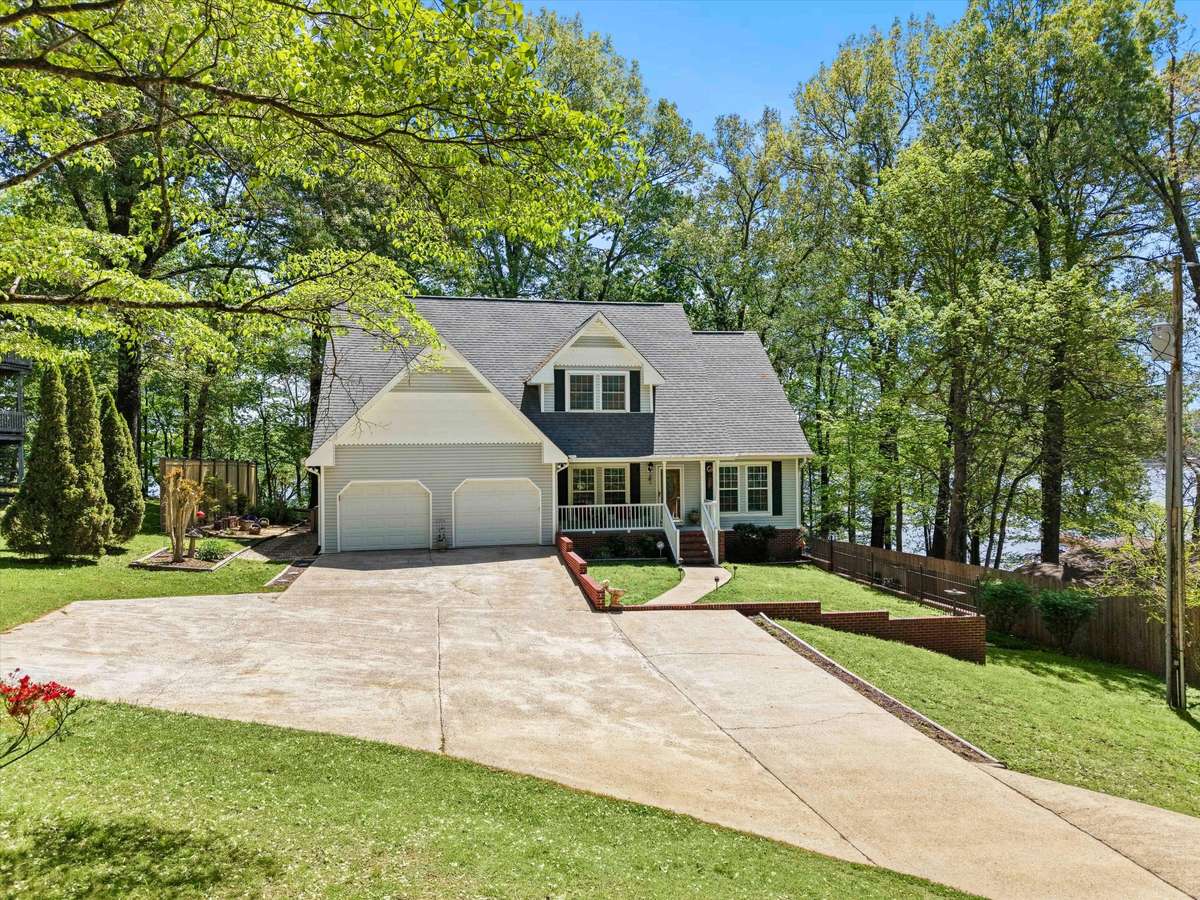 Front of house- Vinyl house, concrete driveway and sidewalks, covered front porch with railing and home entry, two car attached garage, shaded yard beautifully maintained yard