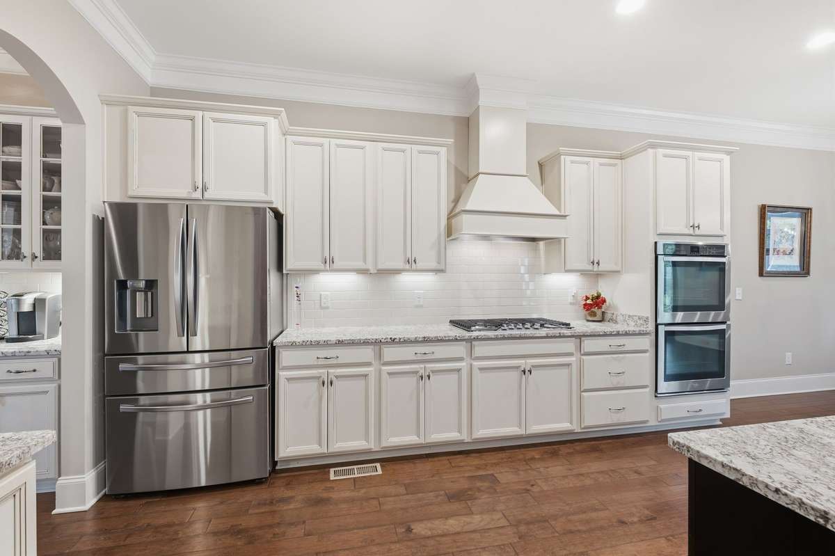 Spacious Kitchen with White Cabinets, crown molding, Gas cooktop with custom hood, double ovens, Breakfast Bar and finished wood floors.