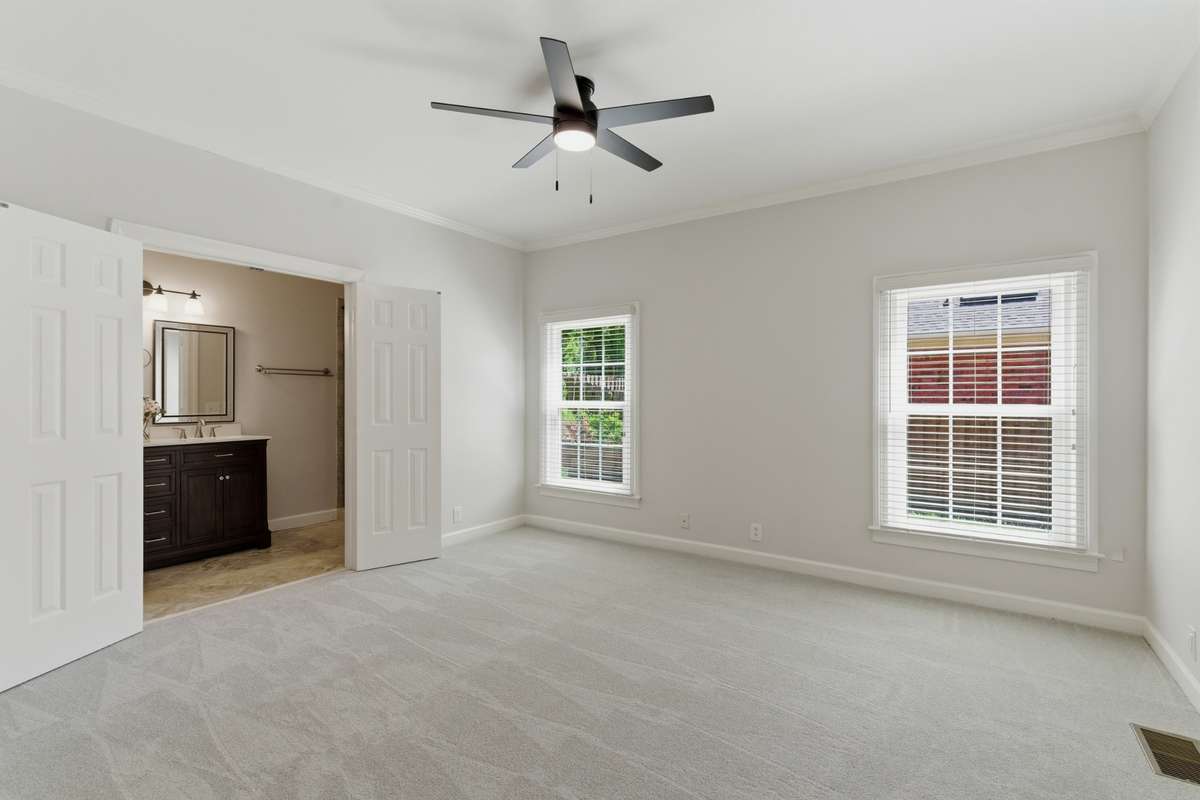 Desirable main-level primary suite with well-appointed en suite bath showcasing tile flooring, a tiled walk in shower,  dual vanities and a private water closet.