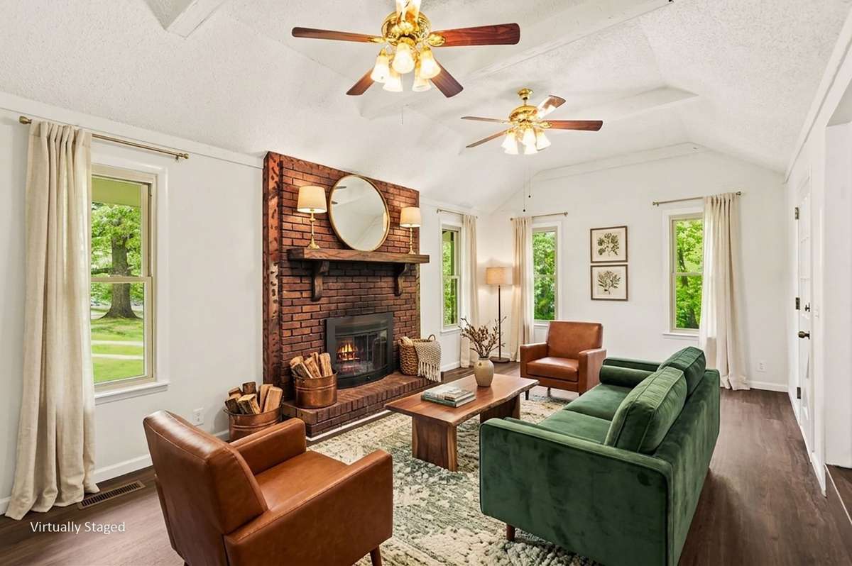 The den is just off the foyer, and features a brick fireplace, cathedral ceilings, large windows overlooking green trees, and two ceiling fans!