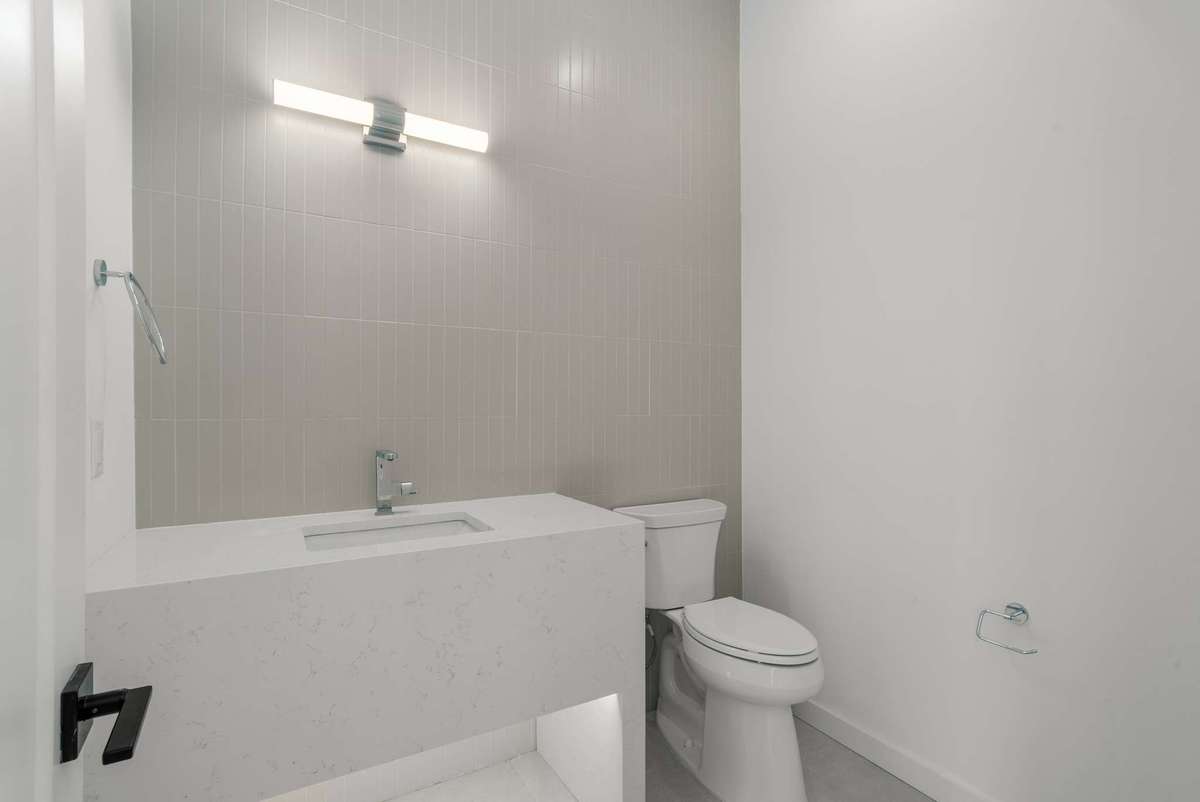 Lower floor powder room by the office with quartz apron vanity and tile wall. Mirror to be selected by the buyer.