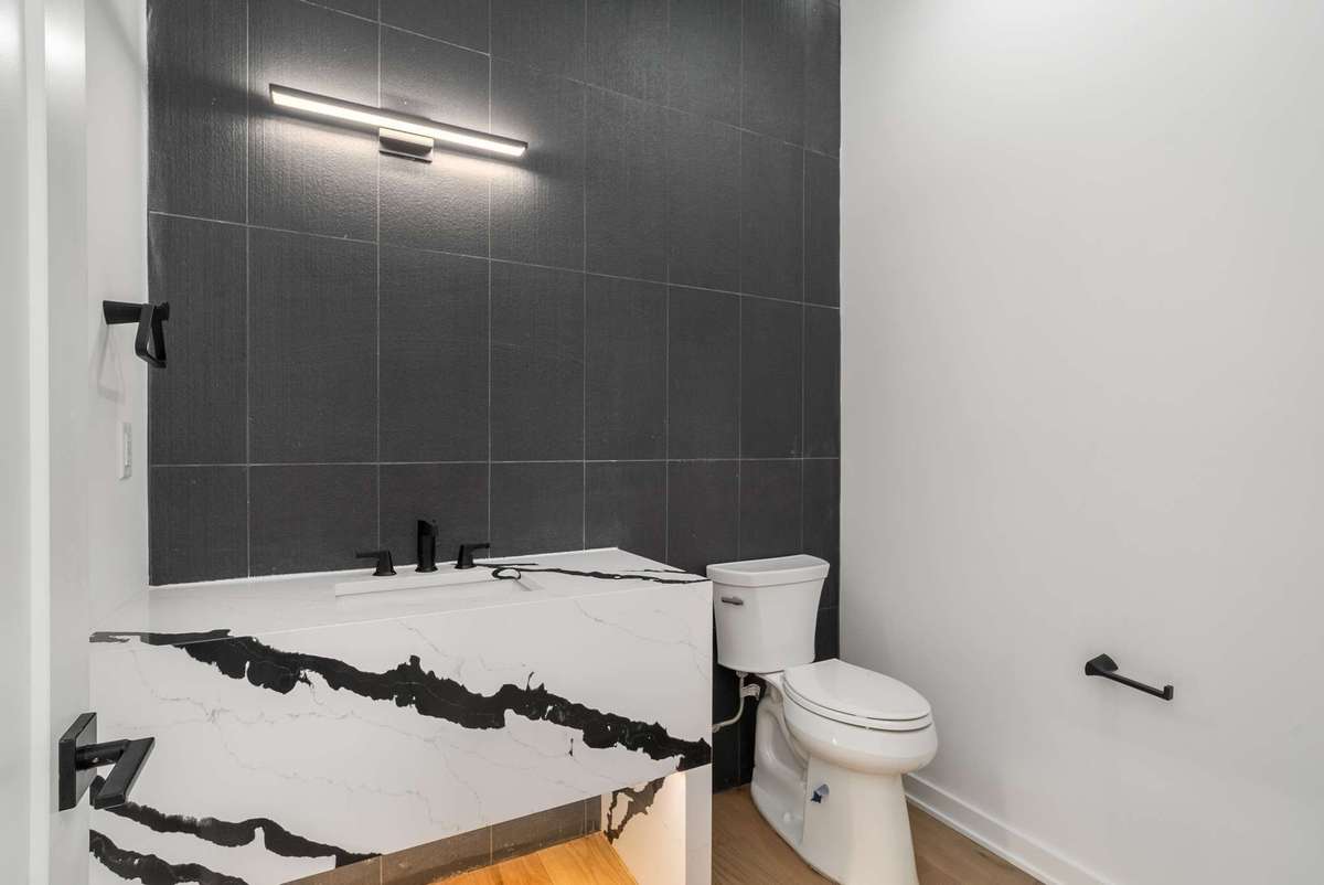 Main floor powder room with quartz apron vanity black tile wall (looks lighter in the photo). Mirror to be selected by the buyer.