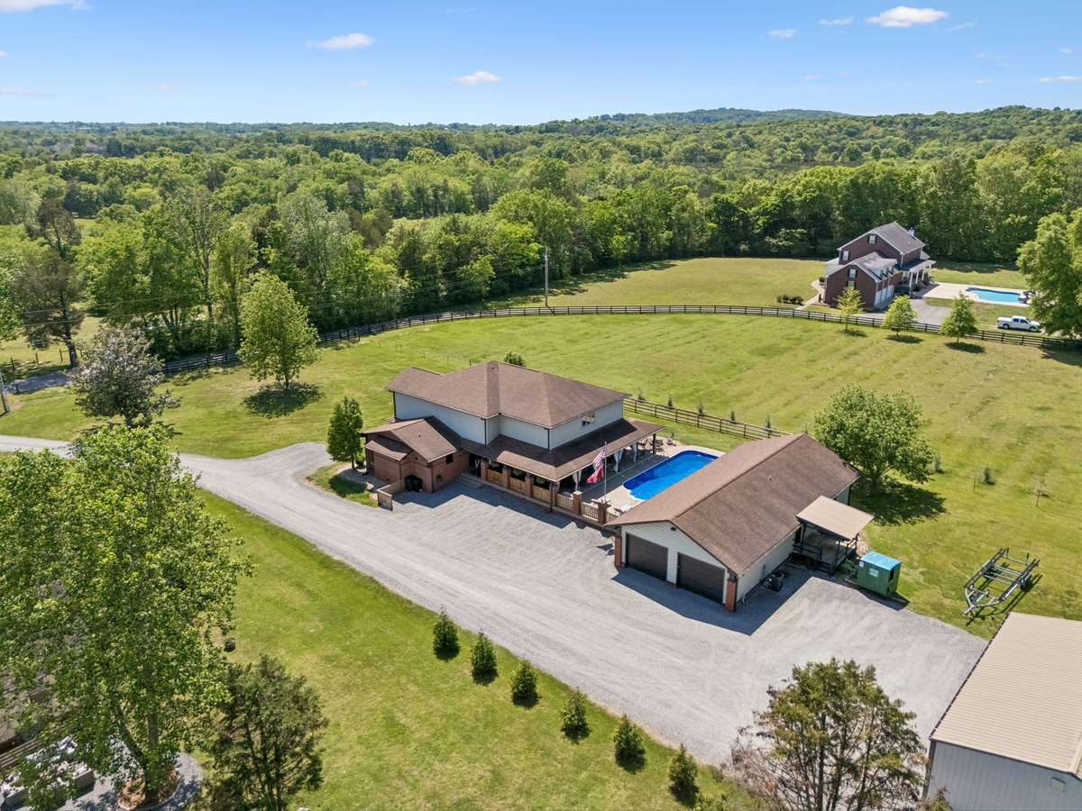 Aerial view of the property showcasing the home, detached garage, in-ground pool, and shop surrounded by scenic countryside.