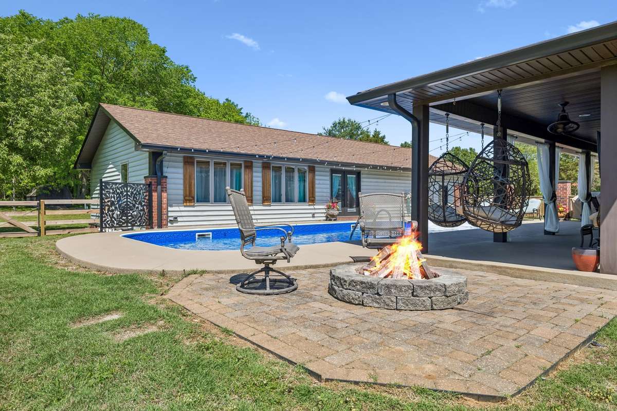Backyard entertaining space featuring a fire pit, covered patio with hanging chairs, and direct access to the pool area.
