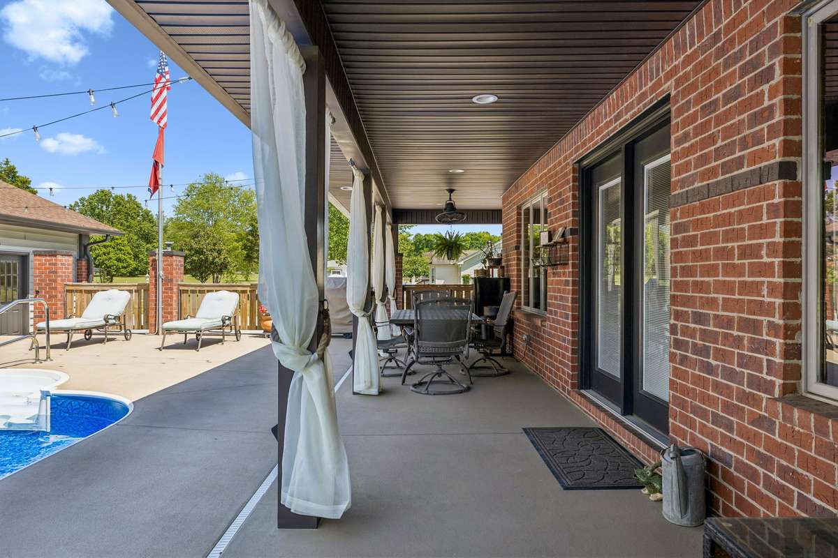 Covered back patio with ceiling fans and seating area, ideal for outdoor dining and enjoying the poolside setting.