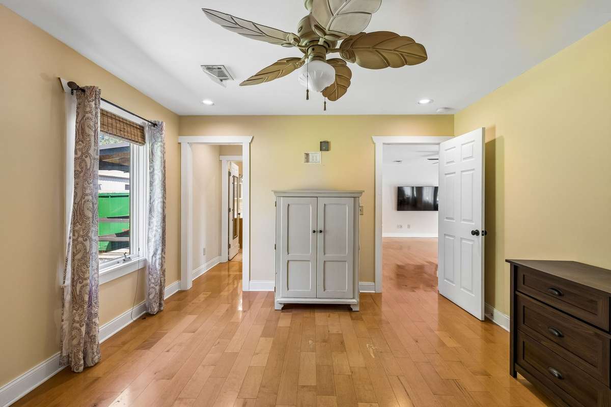 Guest house. Spacious bedroom layout with hardwood flooring, ceiling fan, and flexible space for furniture placement.
