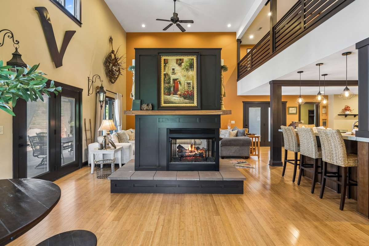 Dramatic two-story great room showcasing a floor-to-ceiling fireplace, accent wall, and access to outdoor living through double doors.