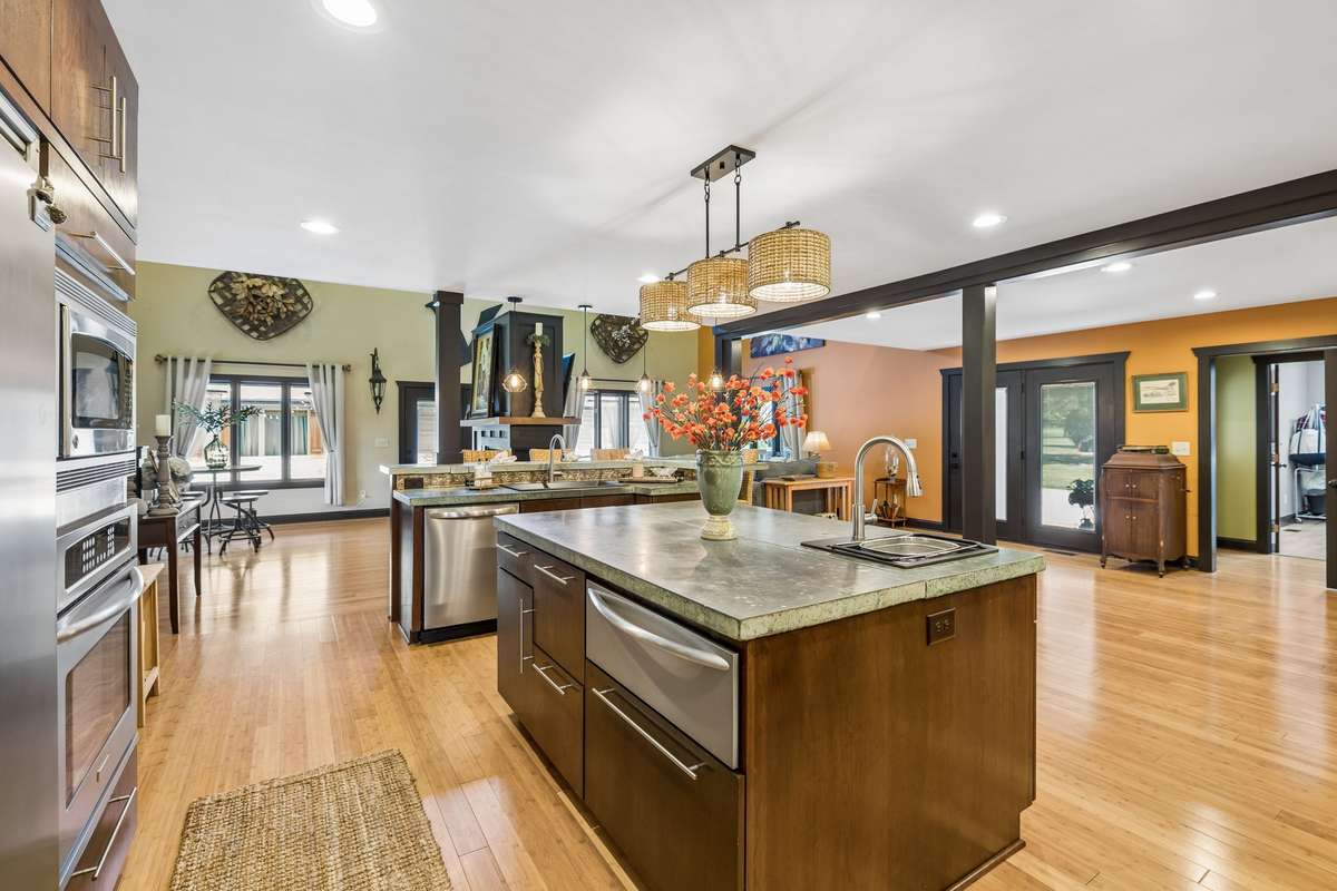 Updated kitchen featuring custom wood cabinetry, concrete countertops, stainless steel appliances, and double wall ovens. Spacious layout with large center island, pendant lighting, and warm accent colors creating an inviting, functional space.