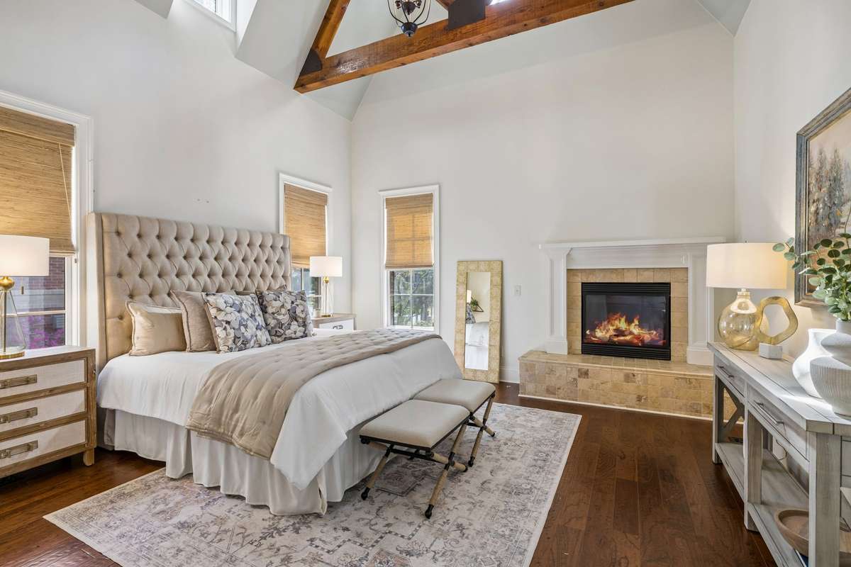 The main-level primary suite is a true retreat, complete with a vaulted ceiling accented by wood beams and a cozy gas fireplace, creating a peaceful and inviting escape.