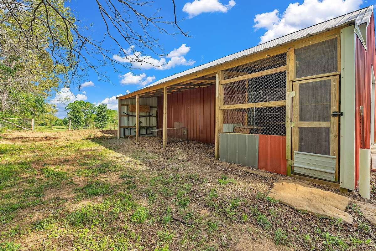 Functional lean-to addition with screened chicken coop, wooden framing, and covered storage space. Complete with water and electricity hookups—ready for animals, equipment, or projects. Surrounded by open pasture and woods on your private mini farm