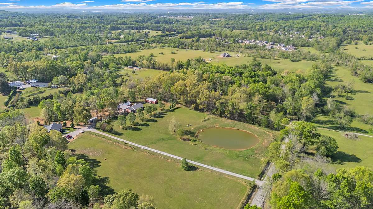 From this breathtaking drone perspective, the entire 5.8 acre paradise unfolds—your private pond sparkling in the center, lush pastures, and the red barn nestled among the trees.
