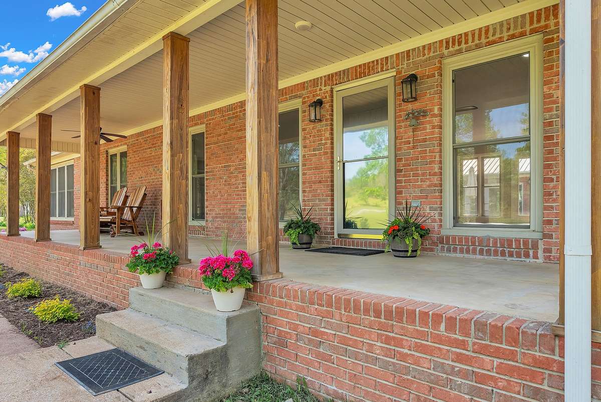 Inviting covered front porch with sturdy wooden columns, concrete seating area, and vibrant appeal for all your future decorations. Classic brick exterior with ceiling fans and rocking chairs ready for relaxing evenings