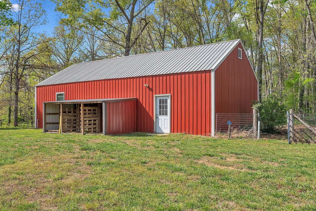 Built in 2021, features a large open bay, concrete floor, 220-amp outlet, dedicated storage, workbenches, shelving, and loft storage with stairs and lighting. Includes temperature-controlled attic fan, firewood lean-to, and water/electricity