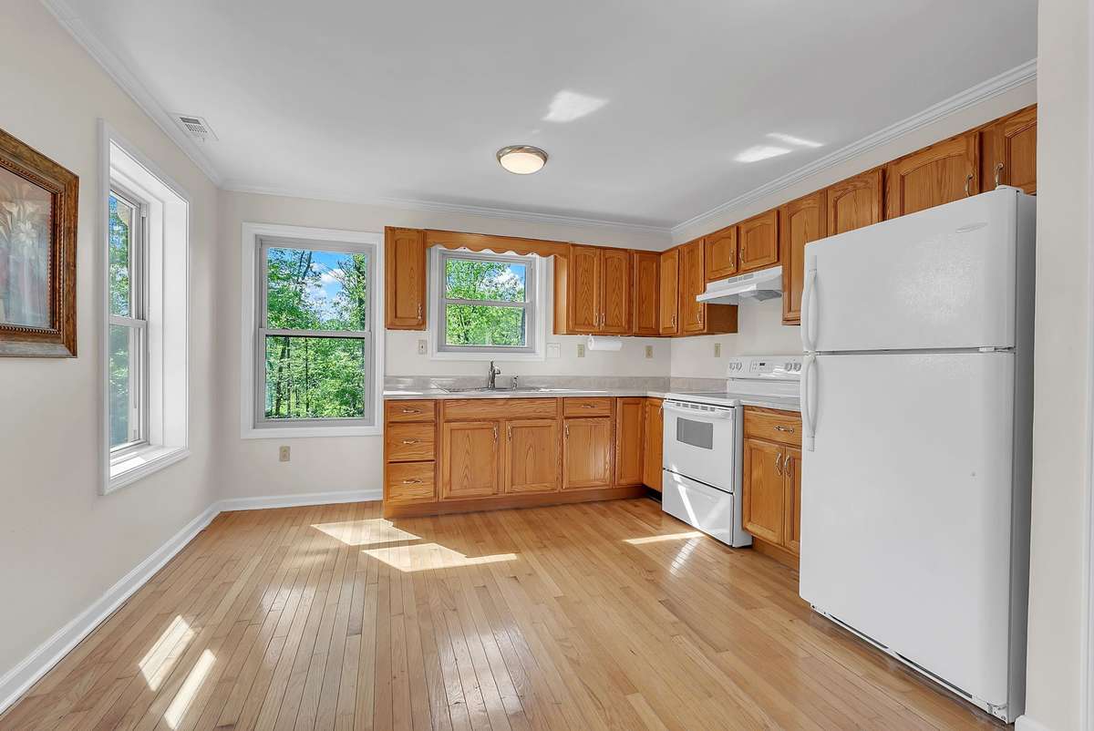 Mother-in-law apartment: Functional kitchen in the in-law suite with warm oak cabinets, granite counters, stainless appliances, and abundant natural light from large windows overlooking the trees. Ideal for independent living.