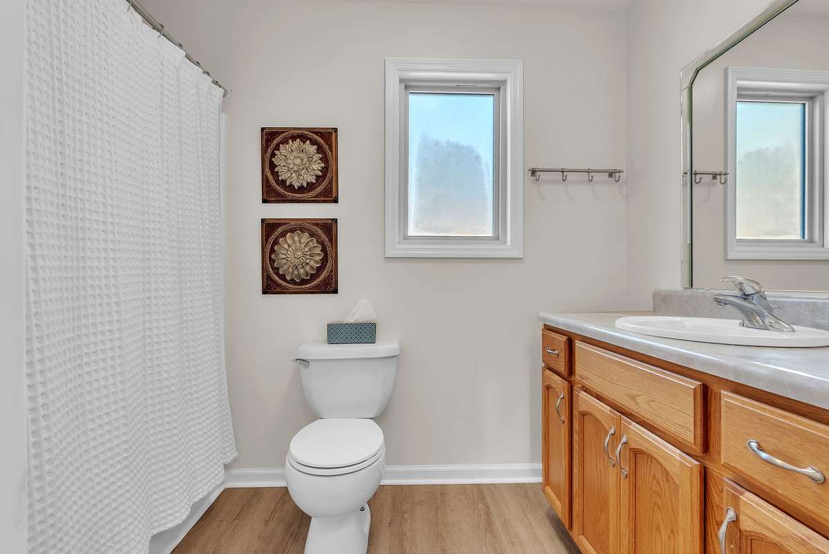 Mother-in-law apartment: Bright, clean full bath in the in-law quarters featuring wood vanity with granite top, large mirror, walk-in shower with white curtain, and neutral finishes. Private and move-in ready for guests or extended family.