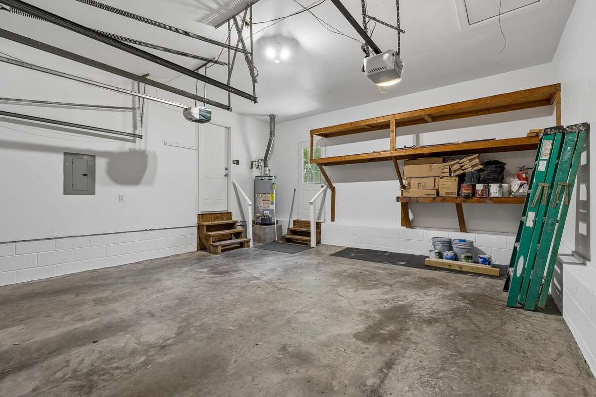 Another view of garage showing shelving/storage space and stairs into kitchen as well as stairs into the backyard.  (Ladder on right not included.)